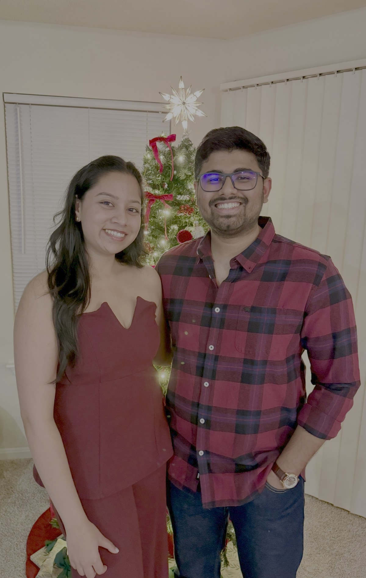 Dakshinya and Karthik smiling together in front of their Christmas tree at home
