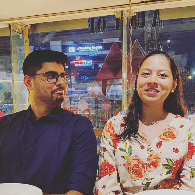 Dakshinya in a floral top and Karthik in a navy shirt sitting together at a restaurant table