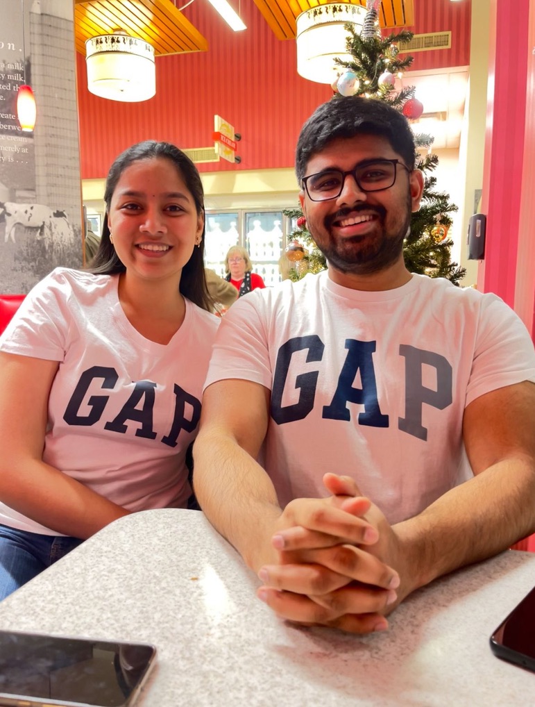 Dakshinya and Karthik in matching GAP t-shirts, smiling together at a café table