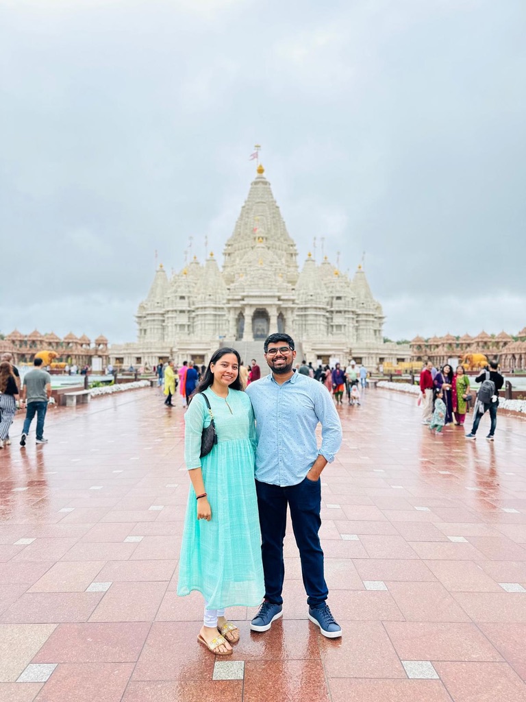 Dakshinya in a teal dress and Karthik standing together in front of a grand white marble temple