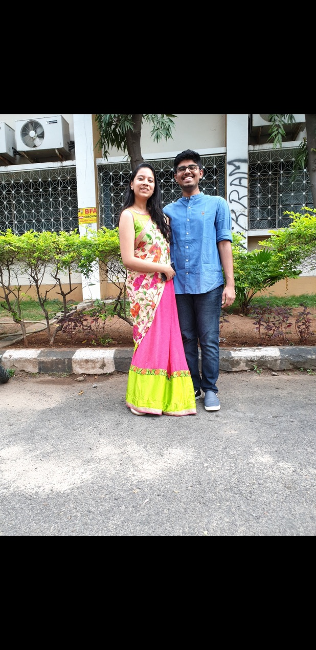 Dakshinya in a pink and green traditional outfit and Karthik in a blue kurta, standing outdoors together